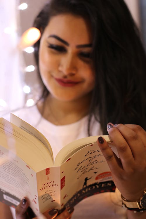 Free Woman Wearing White Crew-neck Shirt Holding Jojo Moyes Book Stock Photo