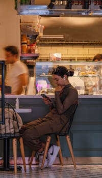 A young woman sitting in a café, using her smartphone while enjoying a relaxed atmosphere.