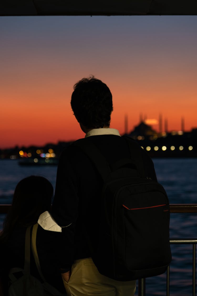 Person Standing Near A Body Of Water At Sunset