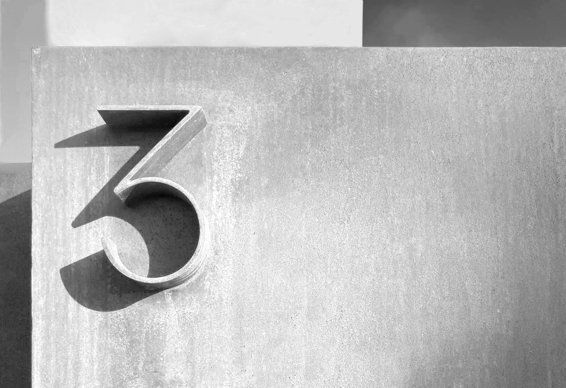 Close-up of the number three in monochrome on a textured concrete background.