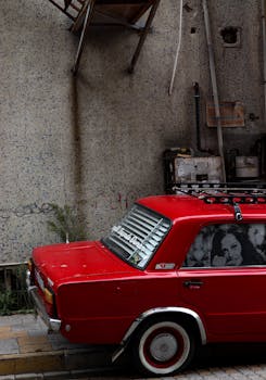 A bright red classic car parked by an industrial wall, showcasing retro vibes and urban setting.