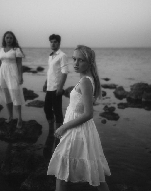 Artistic black and white photo of three people standing on rocks by the sea.