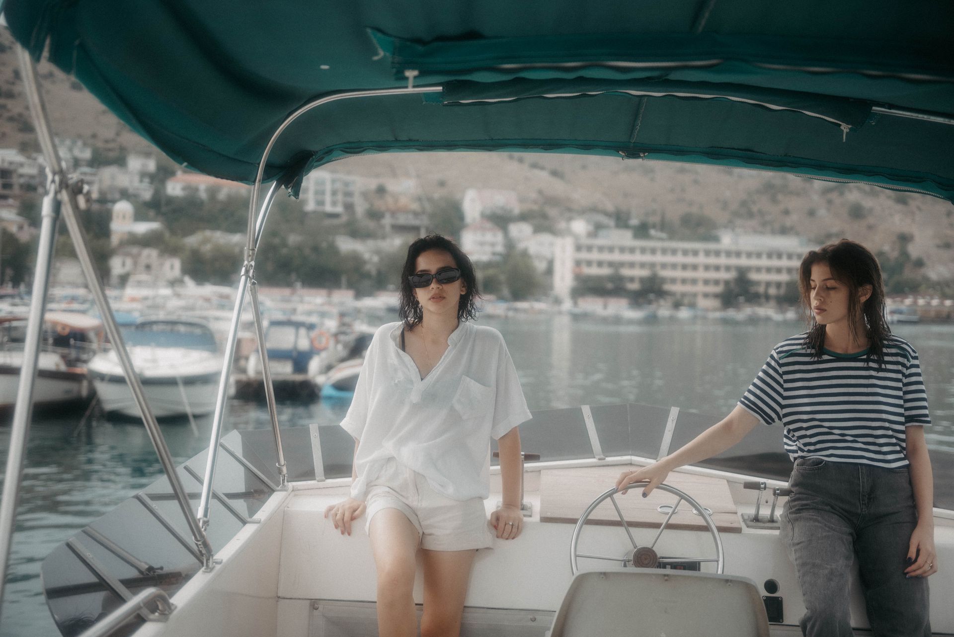 Two women relaxing on a boat with a scenic view of the harbor and mountains in the background.