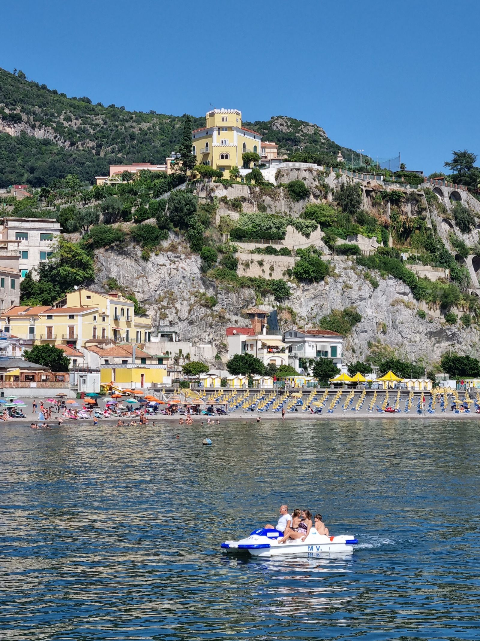 Beach umbrellas and cliffside houses along the waterfront of an Amalfi Coast town
