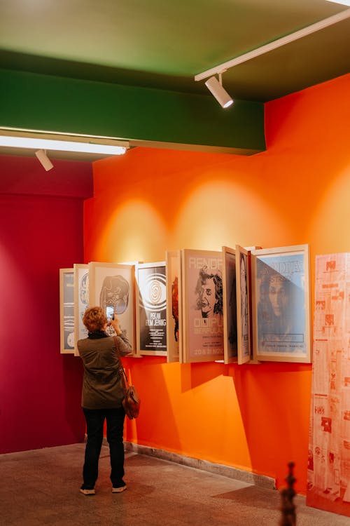 Woman in Green Jacket Taking Picture of Posters on Wooden Frame