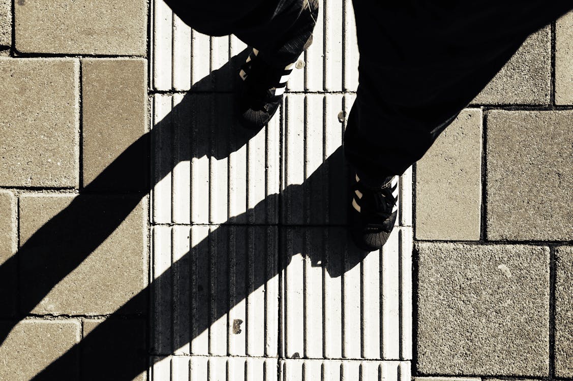 Gratis Orang Yang Mengenakan Sepatu Hitam Putih Berjalan Di Jalan Pada Siang Hari Foto Stok