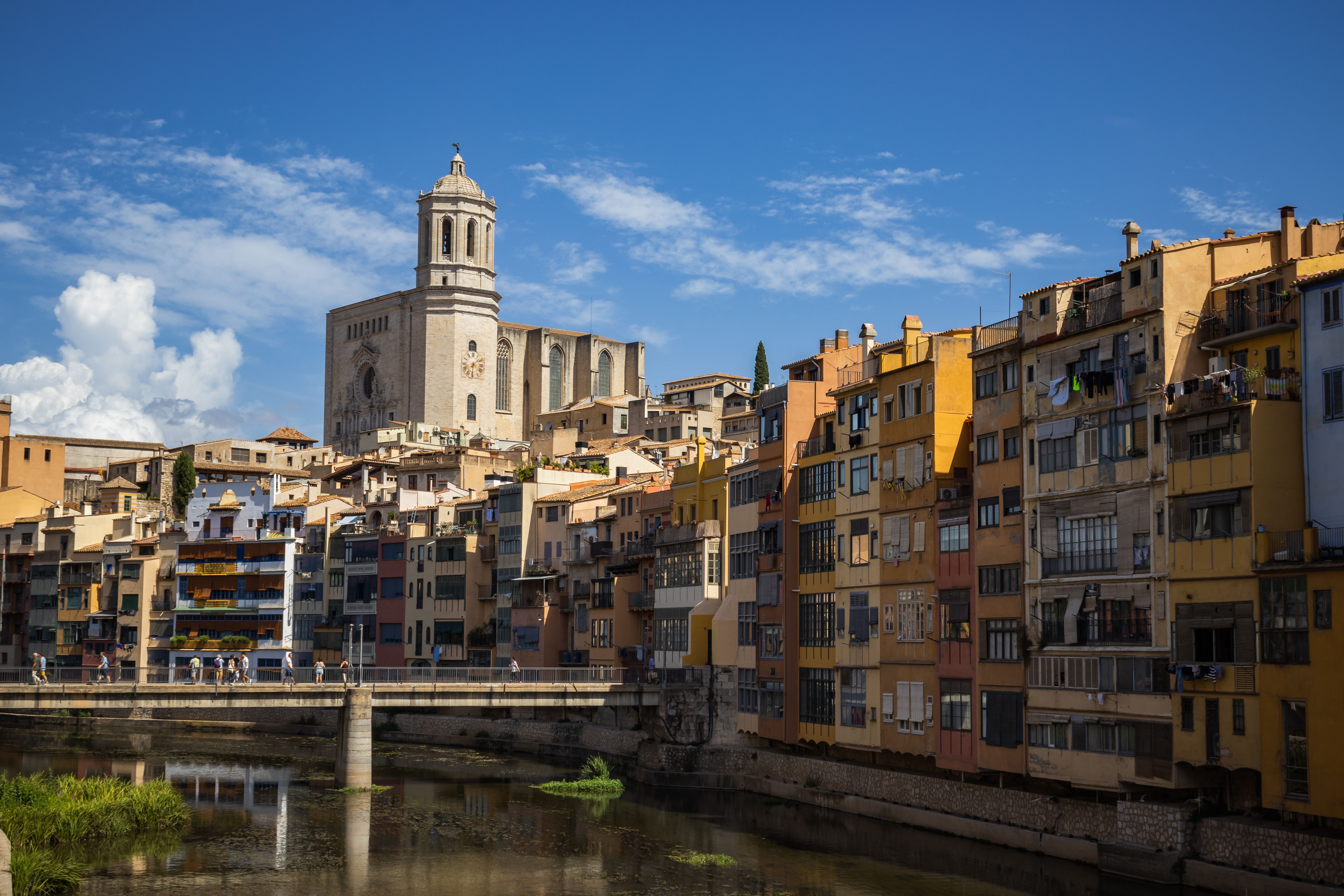 Explore the historic architecture and vibrant colors of Girona, Spain, along the Onyar River under a bright blue sky.