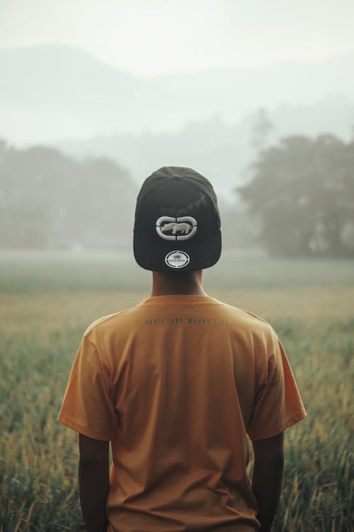 Man in Orange Crew Neck T-shirt Wearing Black and White Cap Standing on Green Grass