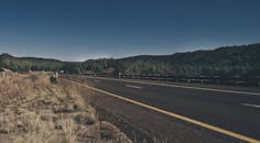 一条高速公路蜿蜒穿过郁郁葱葱的森林山脉，天空蔚蓝