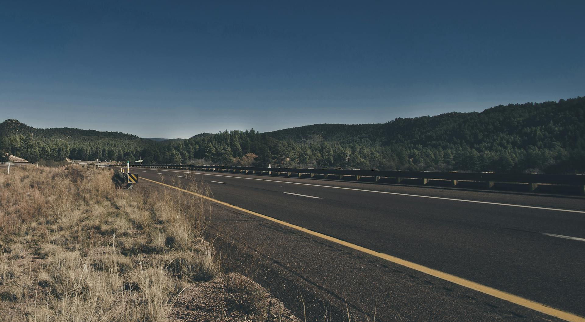 A highway winding through lush forested mountains under a clear blue sky.