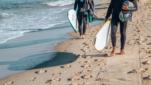 Free Surfers carrying boards along the sandy beach of San Sebastián, capturing a serene seaside moment. Stock Photo