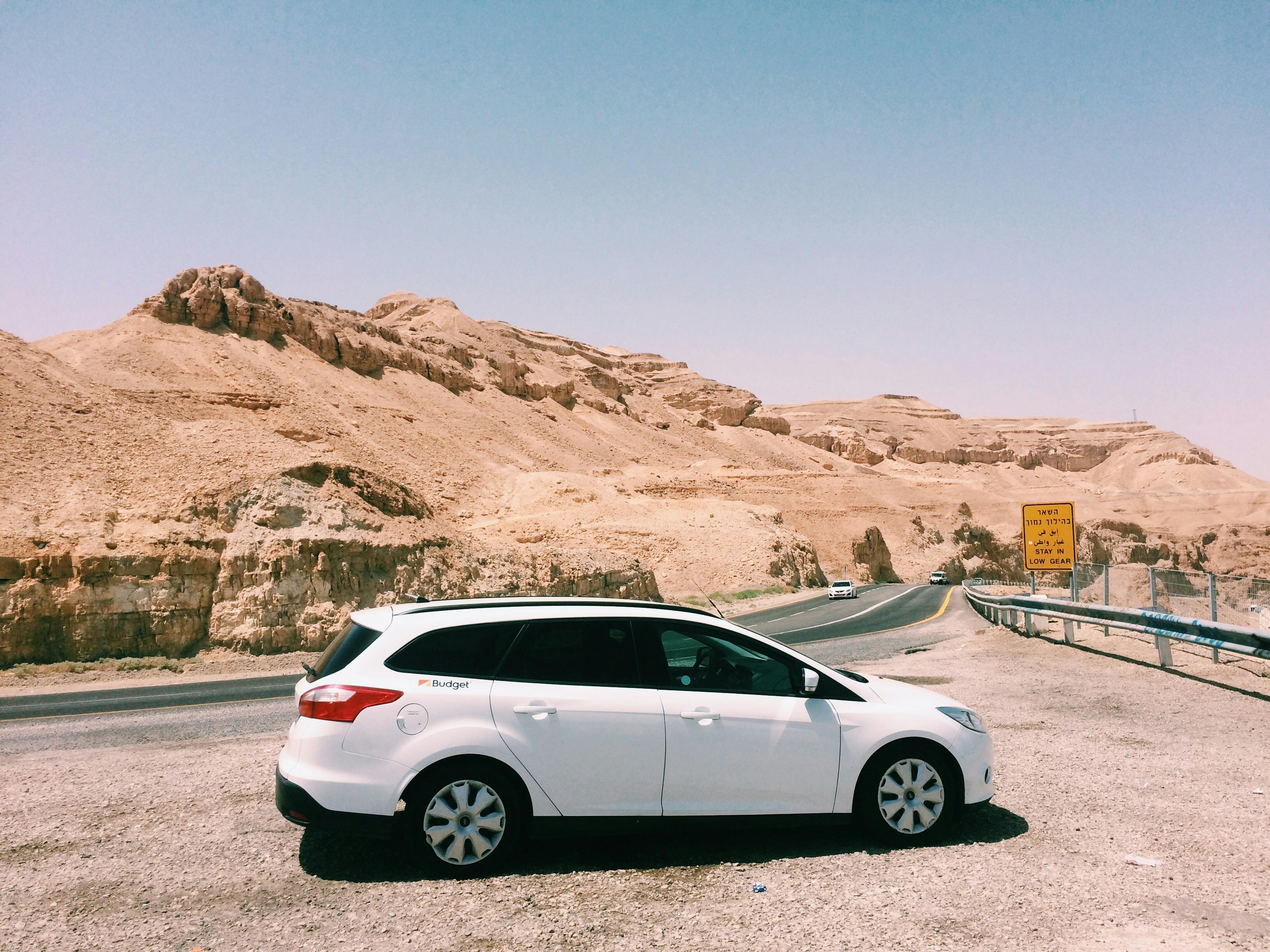 一辆白色汽车停在沙漠公路旁，背景是风景优美的沙漠山脉和清澈的蓝天