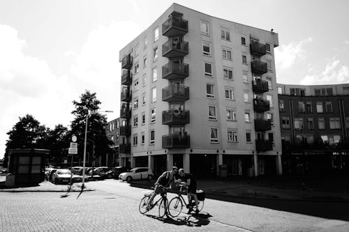 两名男子在建筑物旁边骑自行车的灰度照片