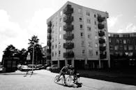 一张黑白照片中，现代城市公寓楼前有人骑着自行车