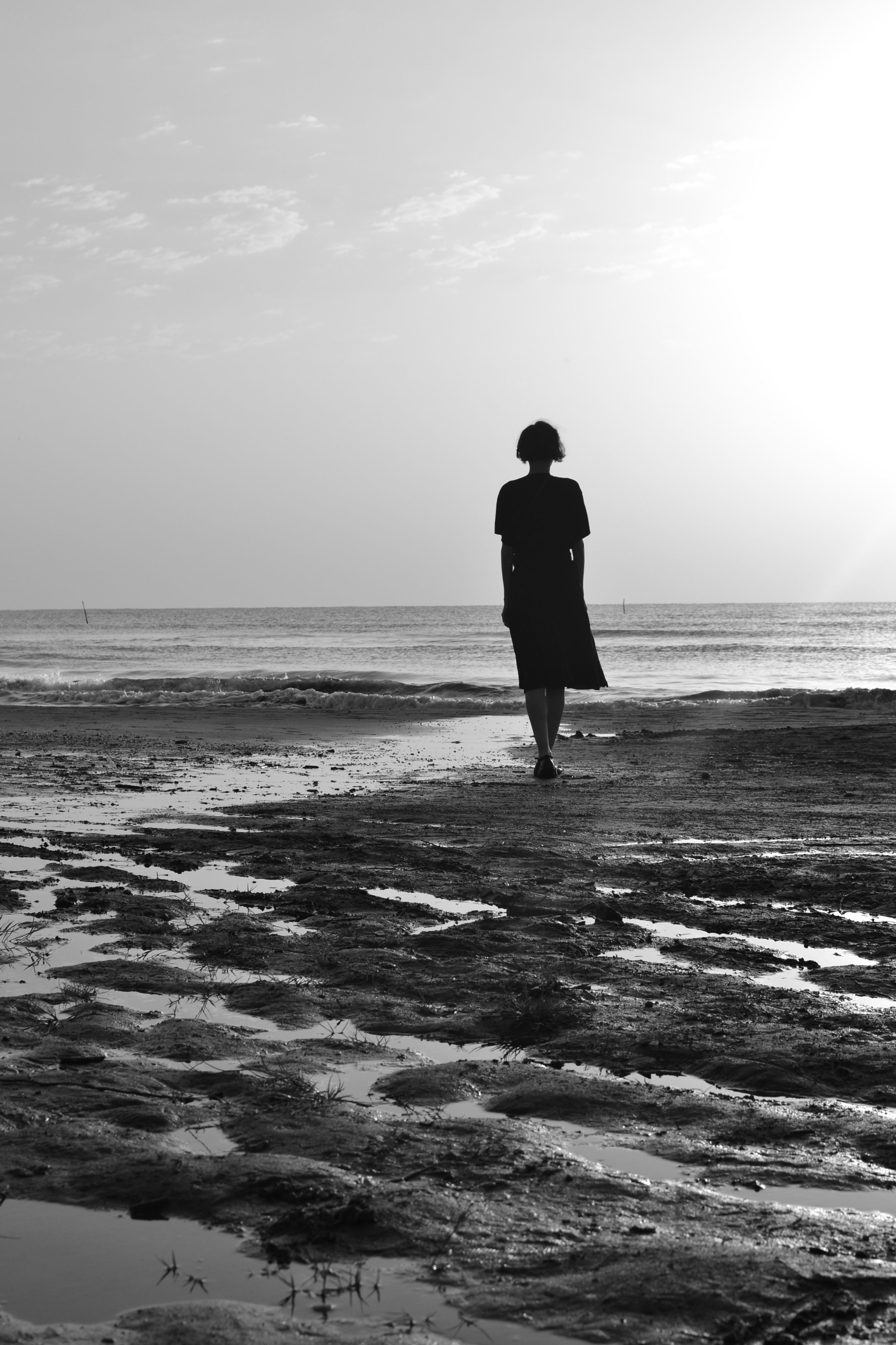 Silhouette of a person walking on a calm beach in black and white, evoking solitude and tranquility.