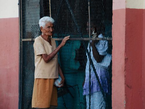 Free A senior woman with white hair standing near a metal fence outside a building. Stock Photo