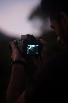 Close-up of photographer taking a picture in low light with DSLR camera.