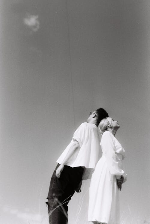 Grayscale Photo of Man and Woman Leaning on Each Other's Back
