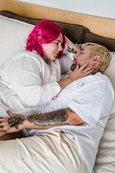 A tattooed couple sharing an intimate moment in bed, full of love and tenderness.
