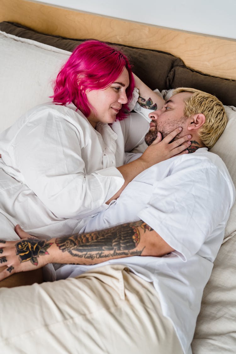 Couple With Tattoos Hugging In Bed