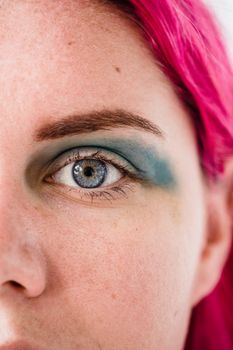 A vibrant close-up shot of a woman's eye with pink hair and blue eyeshadow.