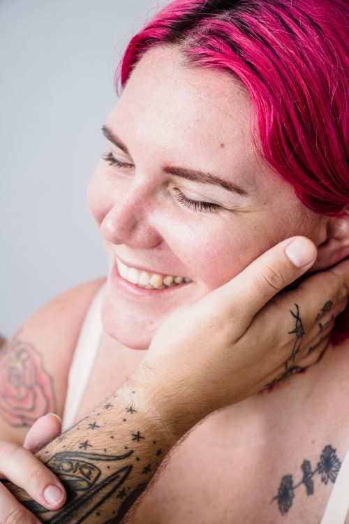 Free Close-up of a smiling woman with pink hair and tattoos, captured in a warm and candid moment. Stock Photo