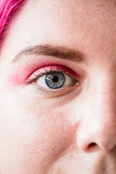 A detailed close-up of a woman's eye featuring bright pink eyeshadow and blue iris.
