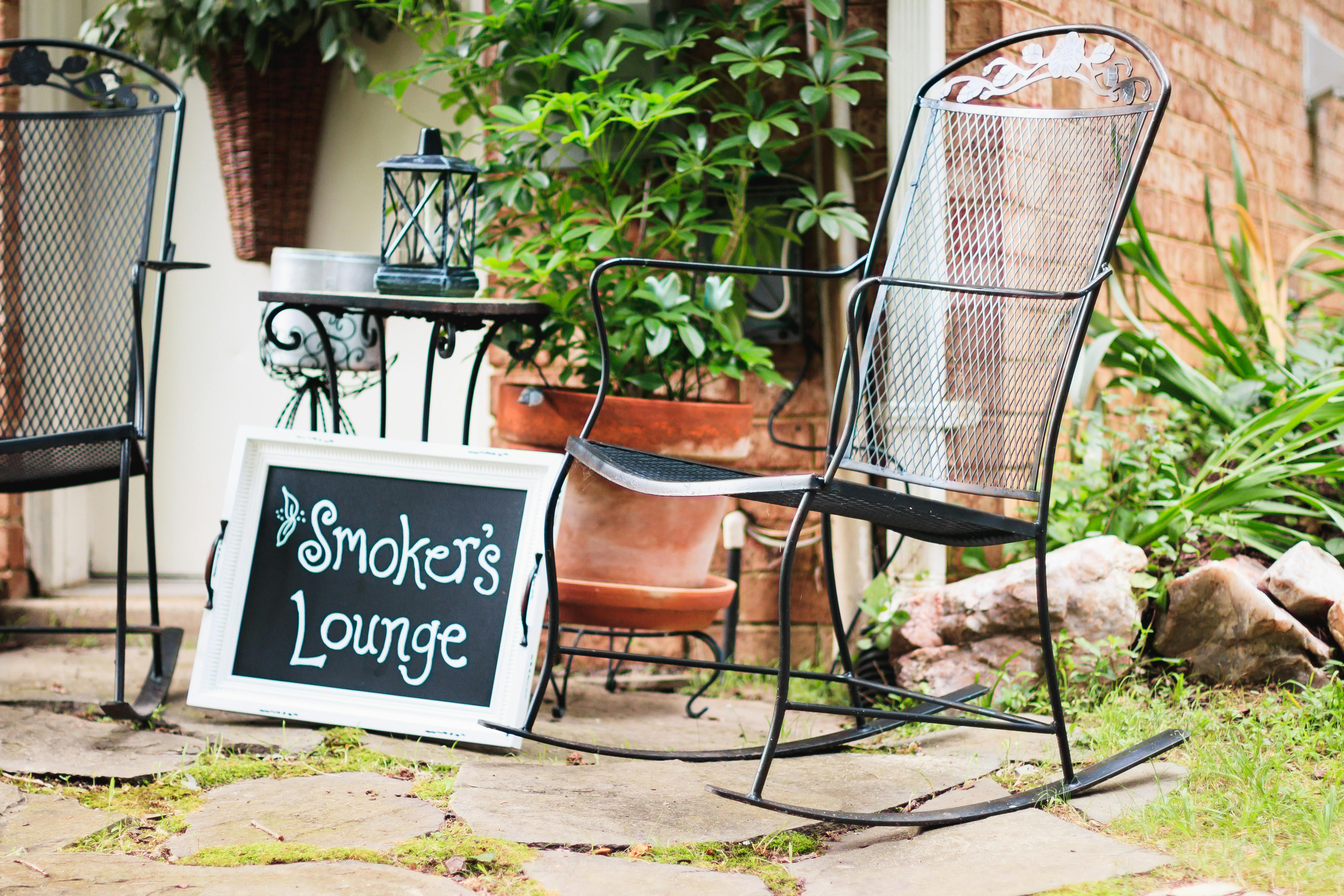 Free Charming outdoor smoker's lounge with metal chairs, plants, sign, and brick wall. Stock Photo