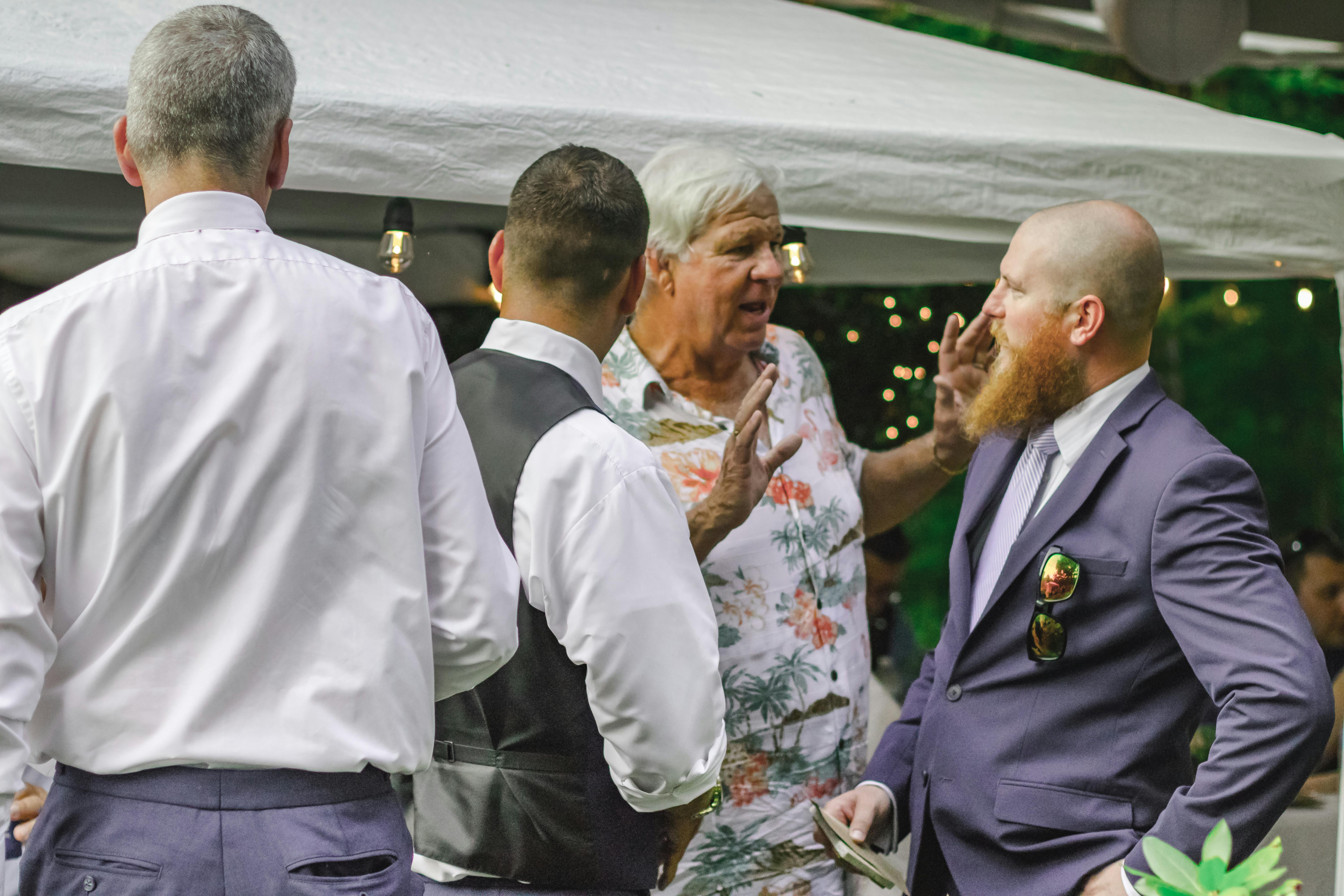 A group of men in conversation at an outdoor event with festive lighting.