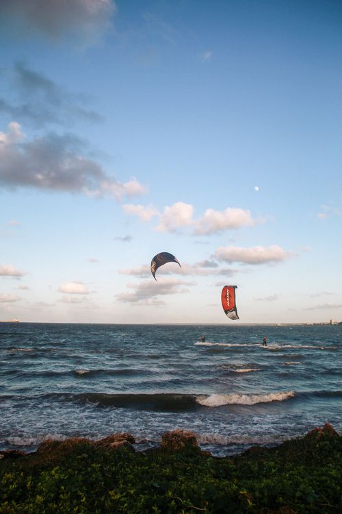 Free Two kitesurfers enjoying an adventurous ride over ocean waves against a stunning sunset sky. Stock Photo