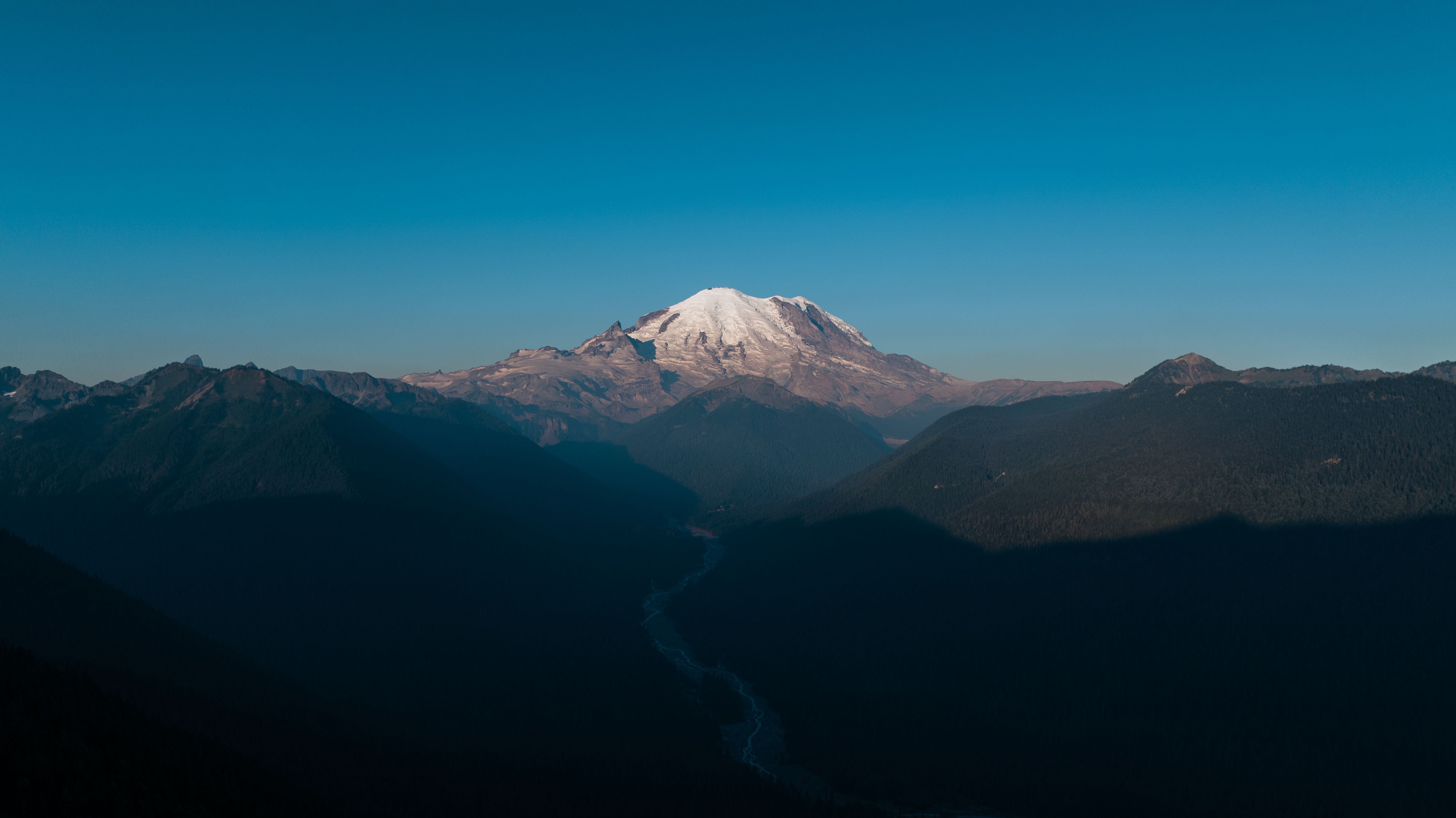 Stunning view of snow-capped Mount Rainier surrounded by valleys under a clear sky.