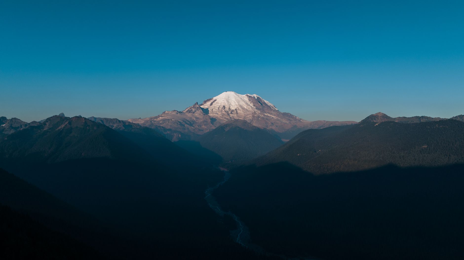 Stunning view of snow-capped Mount Rainier surrounded by valleys under a clear sky.