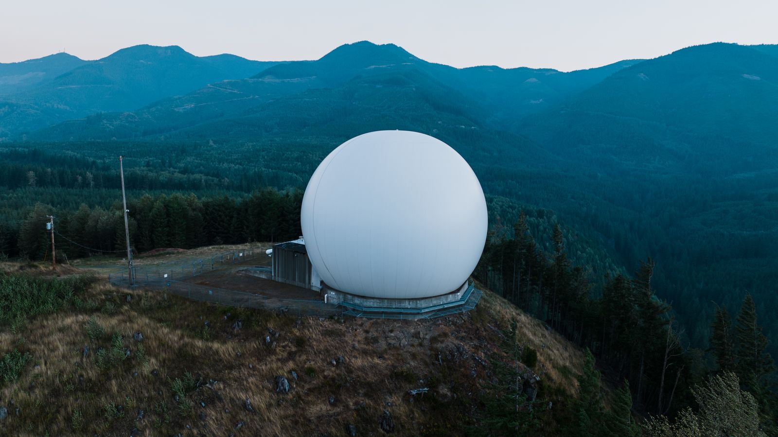 A white radar dome on a forested hilltop at dusk