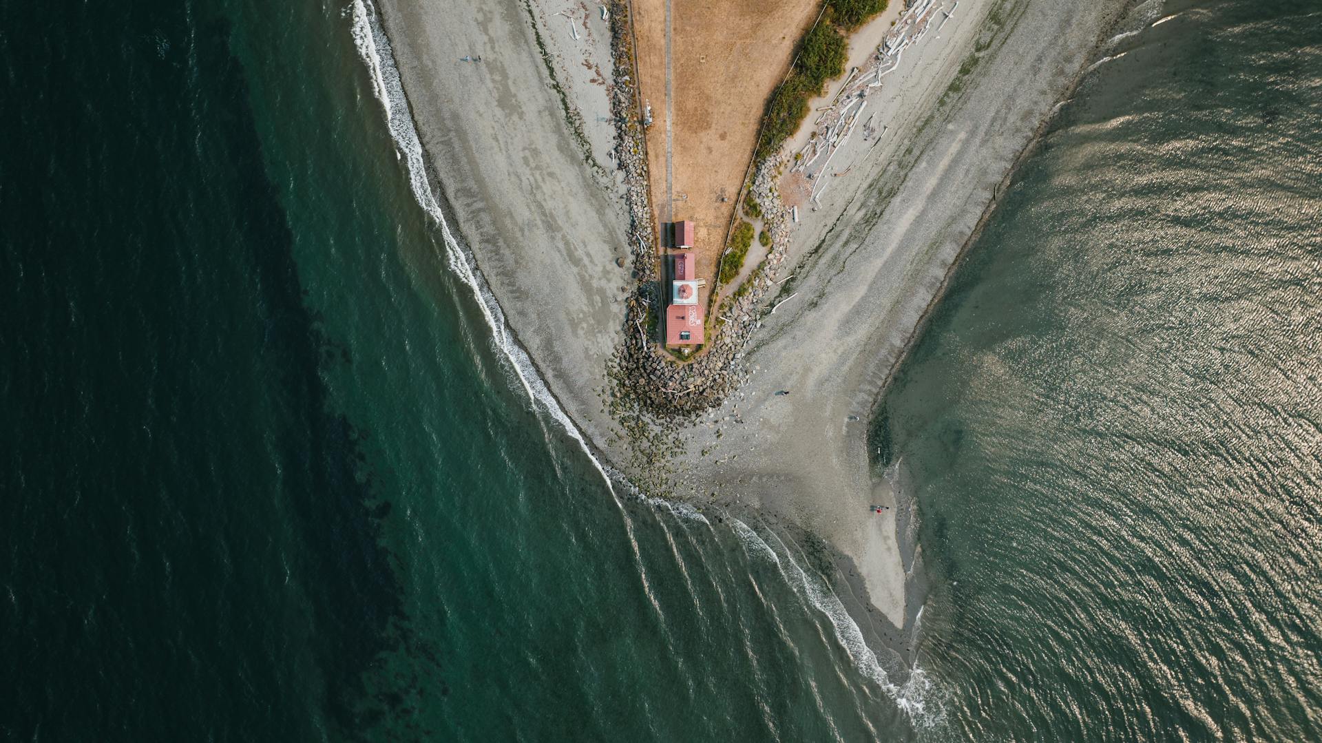 A stunning aerial shot of a lighthouse on the rugged Seattle coastline, capturing the converging land and sea.