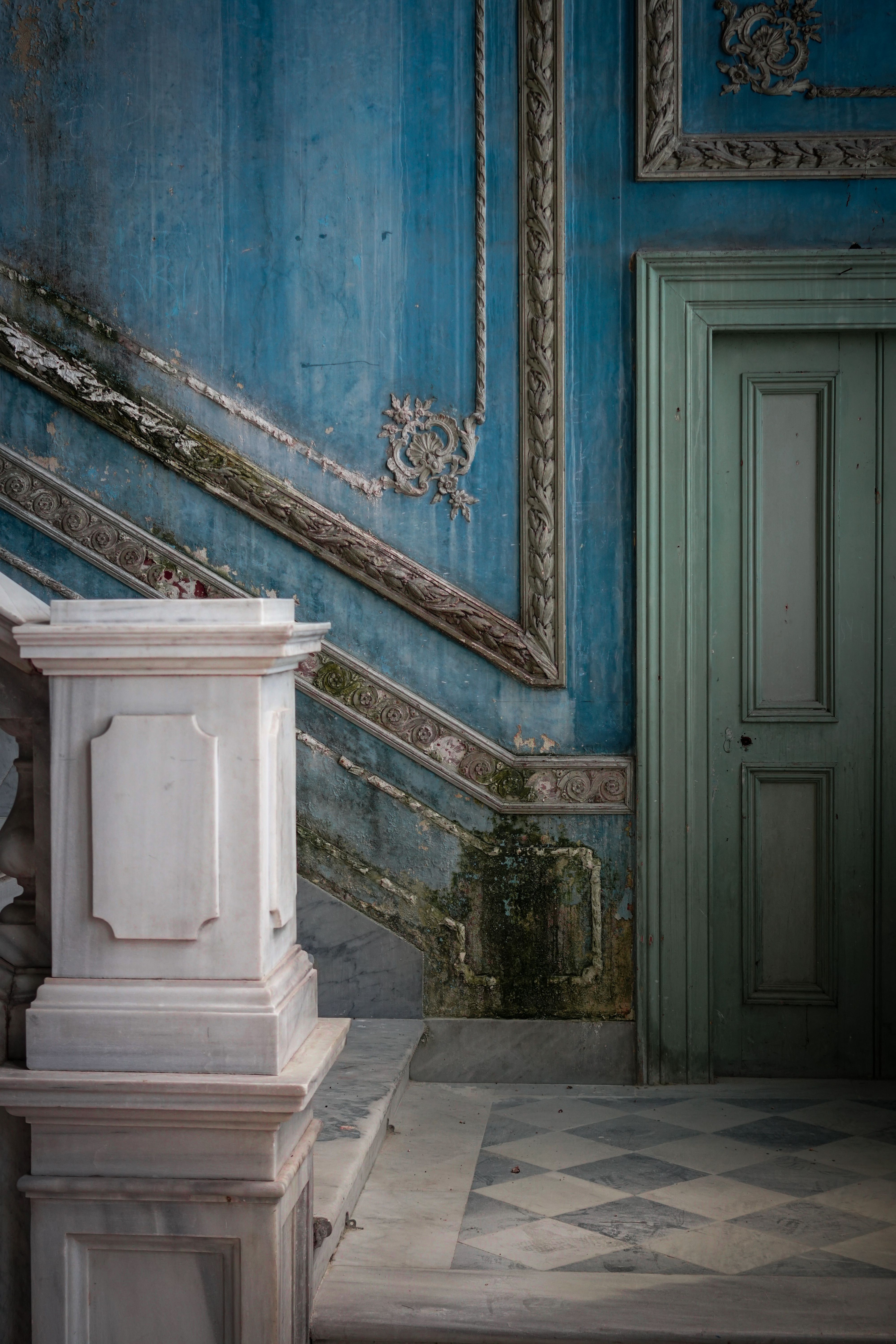 Ornate abandoned interior with blue walls and a green door showcasing classic architectural details.