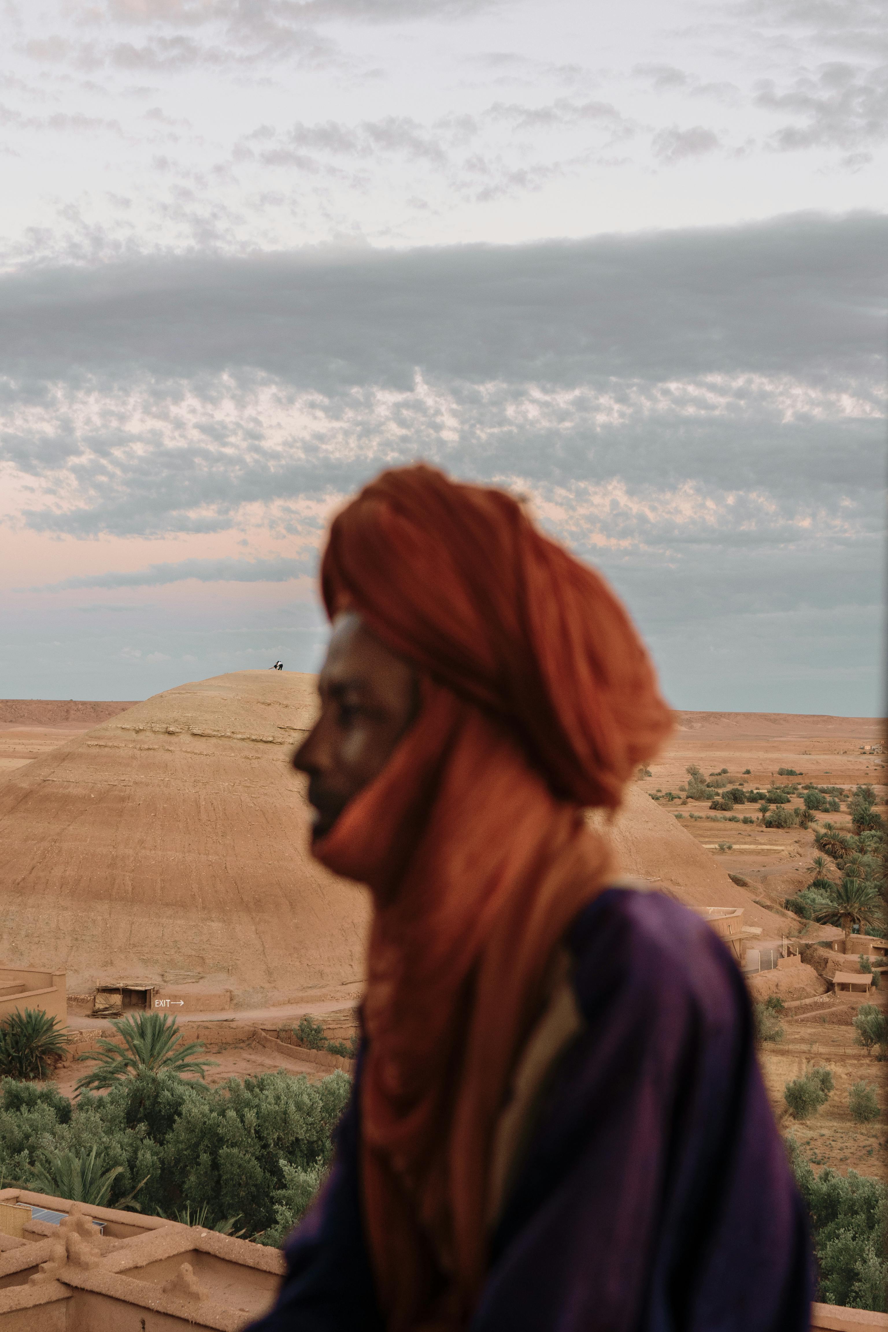 Blurred silhouette of a man in a turban against the backdrop of a desert landscape in Ouarzazate, Morocco at sunset.