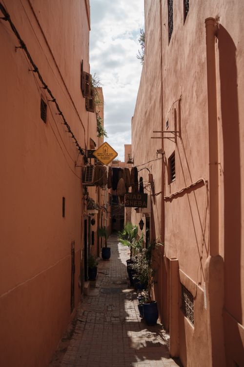 Free A charming narrow alleyway lined with peach-colored walls and potted plants under a clear sky. Stock Photo