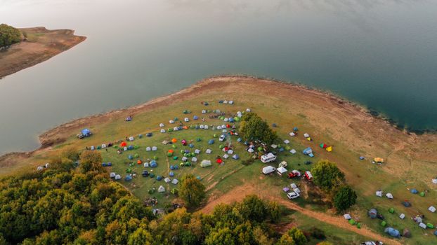 Aerial view of a vibrant lakeside campsite with numerous tents and scenic surroundings.
