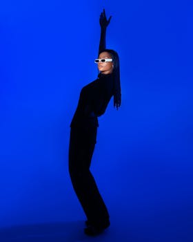 Stylish woman in black outfit posing against a vibrant blue background, showcasing modern fashion.