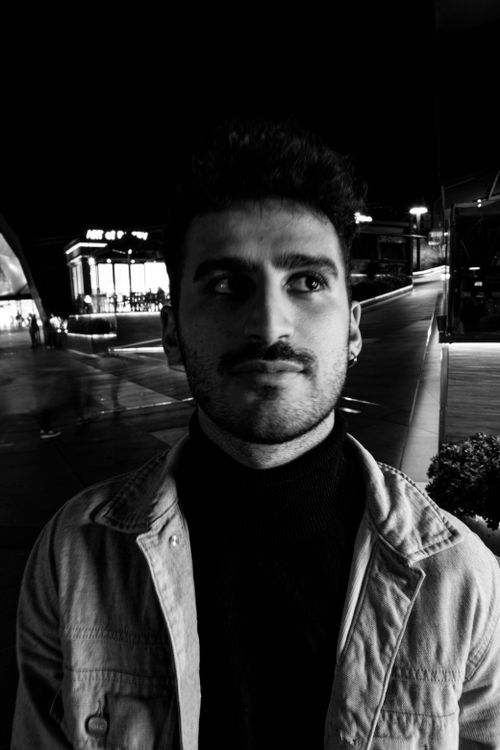 Free Stylish black and white portrait of a young man with facial hair, wearing a jacket, captured at night in an urban setting. Stock Photo