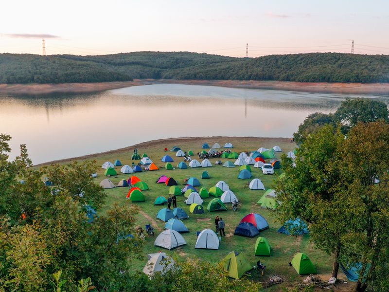 Tents pitched beside a lake at sunset surrounded by greenery