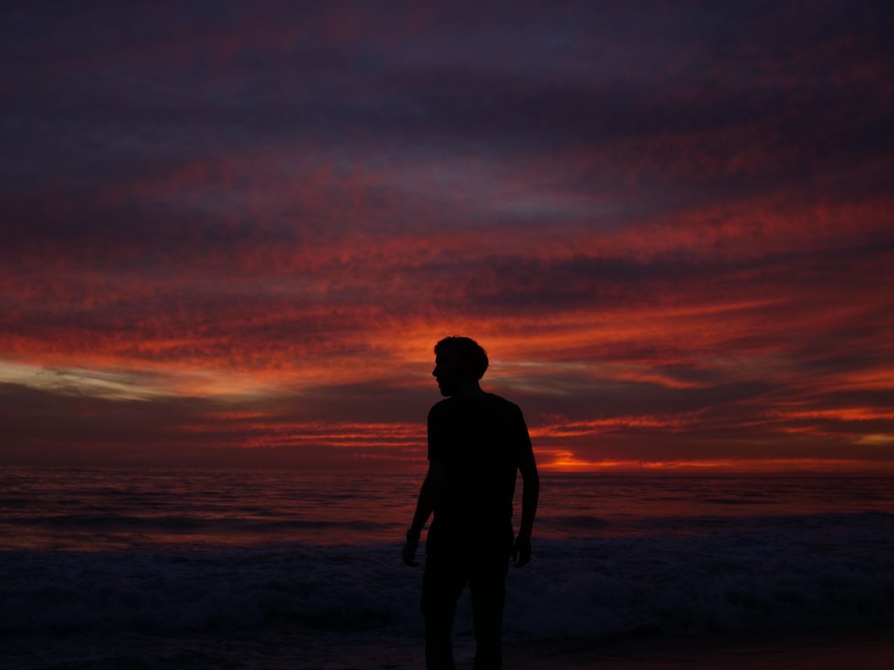 a silhouette of a man stands by the ocean engulfed in a dramatic sunse