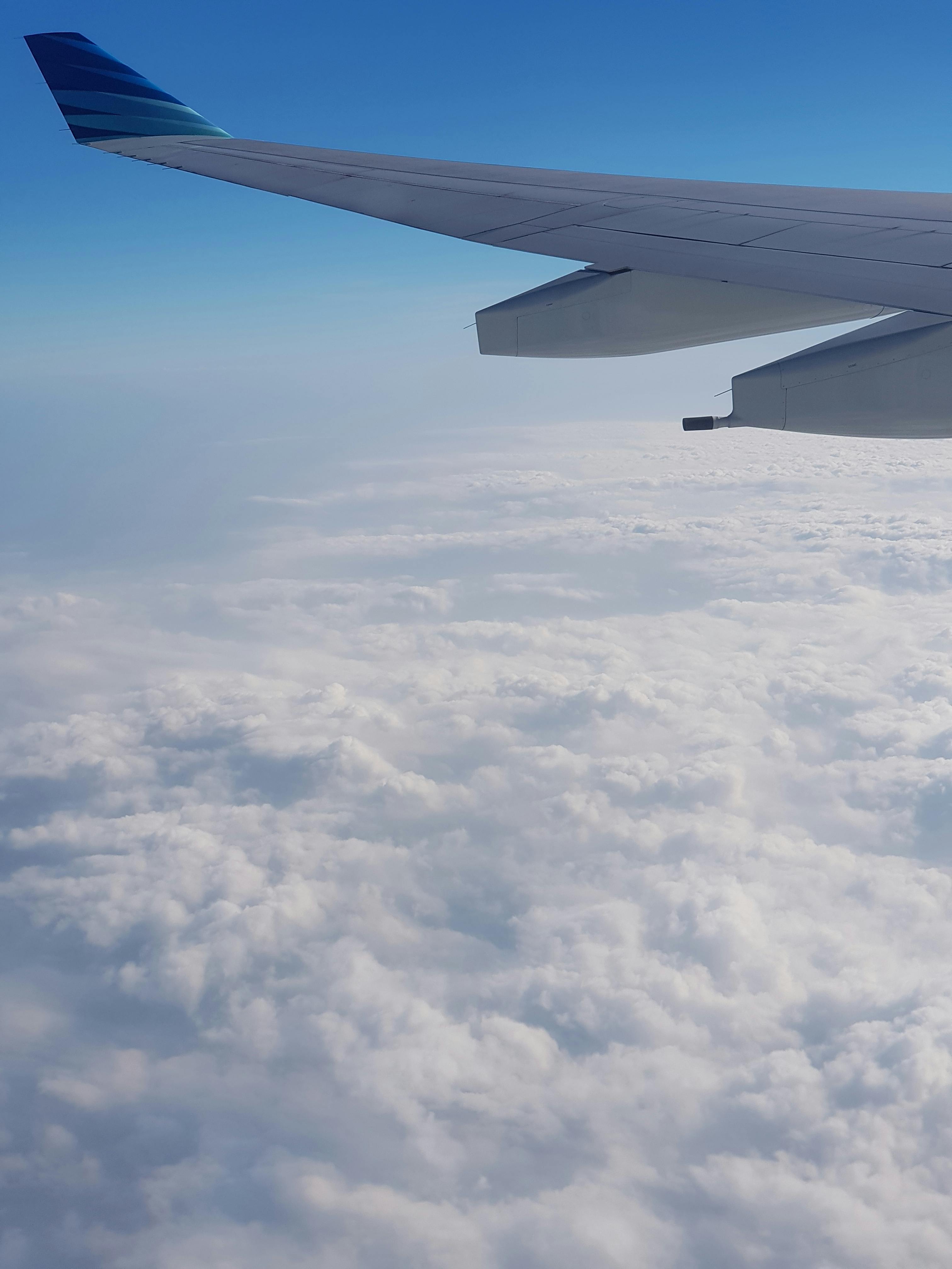 View of an airplane wing soaring above fluffy clouds against a clear blue sky.