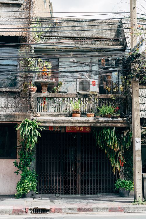 Free An urban facade with a balcony, plants, and exposed wiring under a blue sky. Stock Photo