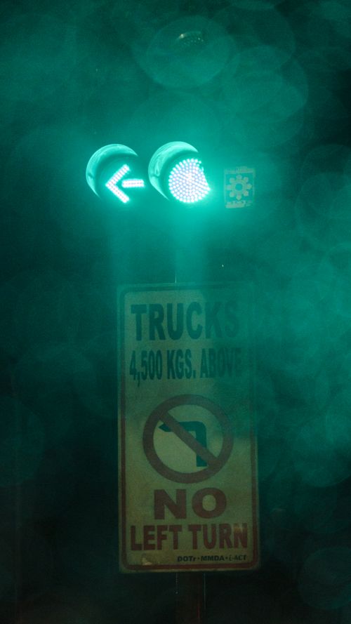 Free Illuminated green traffic signal with a no left turn sign for trucks over 4,500 kgs at night. Stock Photo