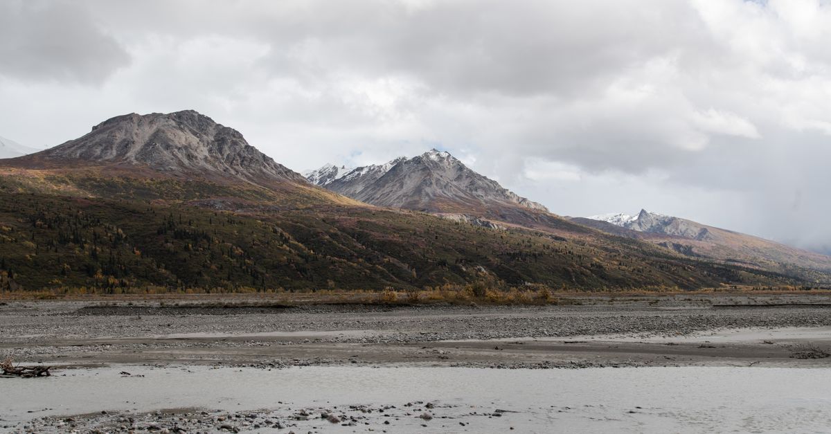 Breathtaking view of Alaskan mountains and river under a cloudy sky, capturing nature's serenity.