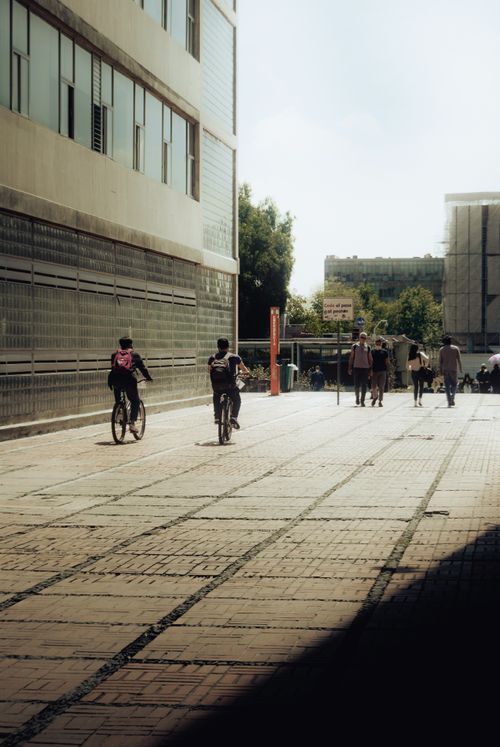 Free A sunlit urban street with people walking and cycling beside modern buildings. Stock Photo