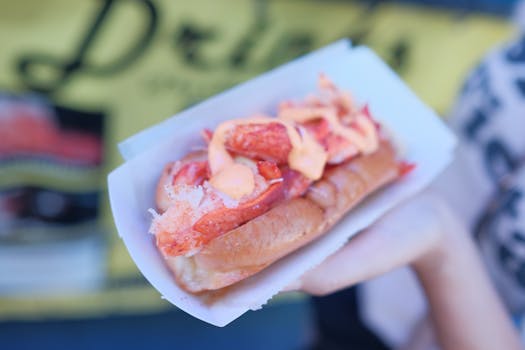 Close-up of a fresh lobster roll on a paper plate held outdoors. Perfect for seafood lovers.