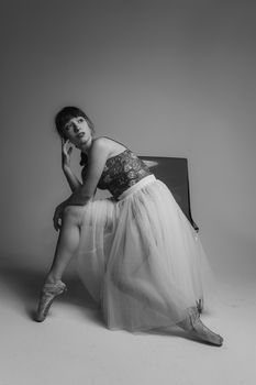 Artistic monochrome portrait of a ballerina in a tutu posing thoughtfully in a studio setting.