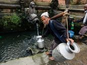 Elderly man filling jars with water from a traditional fountain, showcasing daily life and cultural heritage.